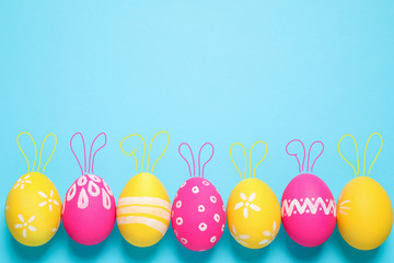 Bright Easter eggs with cute bunny ears and space for text on light blue background, flat lay