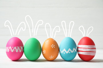 Bright Easter eggs with cute bunny ears on white table