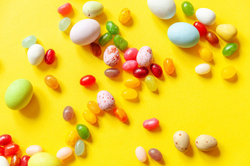 Happy Easter concept. Preparation for holiday. Easter candy chocolate eggs and jellybean sweets isolated on trendy yellow background. Simple minimalism flat lay top view copy space.