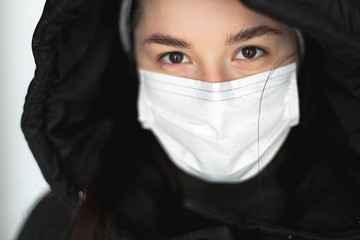 selective focus, noise effect: look of a girl dressed in a medical mask and a hooded jacket