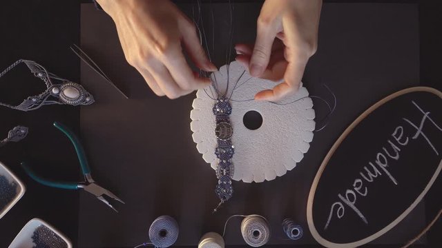 Lifestyle concept, work from home to reinvent your life: close-up of woman hands making macrame knots the gray thread creating a bracelet on kumihimo tools on black work table