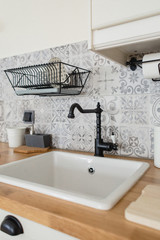 Cozy, bright Scandinavian-style kitchen. White, gray, black. Dishwashing sink, faucet, metal dishwasher, tile with patterns.