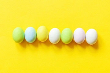 Happy Easter concept. Preparation for holiday. Easter candy chocolate eggs colorful pastel sweets and bunny toy isolated on trendy yellow background. Simple minimalism flat lay top view copy space.