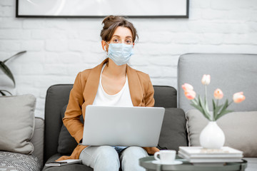 Portrait of a sad woman in medical mask working on laptop online from home. Stay at home during a virus pandemic concept