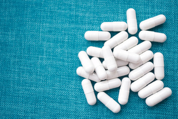 White capsules in bulk on a blue background. Medical theme. Copy space on the left. Place for text.