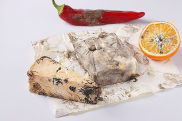 Spoiled rotten foods with mold: orange, pepper, hard cheese and butter on white background