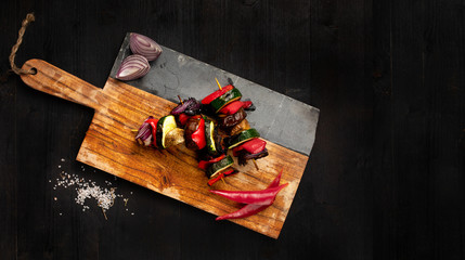 Tasty veggie skewer with onion and pepper aside, isolated on a dark wooden background. Space for text left. Hight contrast product photography done with professional lighting