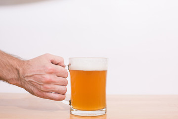 Man holding beer mug full of beer on wooden table on white background