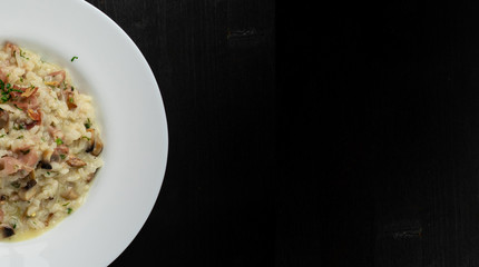 Super clean tatsy risotto with bacon and mushrooms. Round plate and wooden background with space...