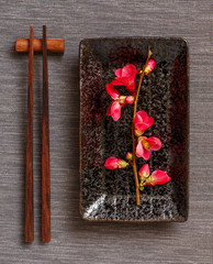 Chopsticks, rectangular plate and pink flowers on gray runner