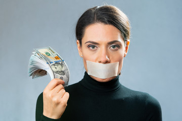 a young lady in black holds in her hand a lot of cash American dollars with banknotes of one hundred dollars, close-up portrait with her mouth closed with a white ribbon.