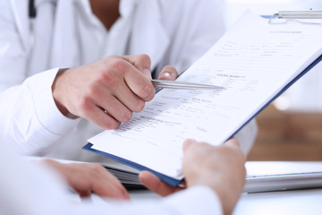 Male doctor hand hold silver pen and showing pad. Physical agreement form signature, disease...