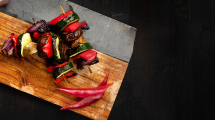 Tasty vegetable skewer on a wooden board with sliced papers aside. Black wooden board with space for text.