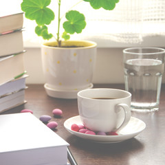 The white paper lies on a wooden table next to a stack of colorful books, a cup of coffee and a pot against