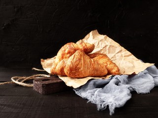 Freshly baked croissants on Kraft paper on a black background with space for text. 