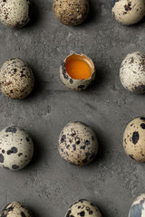 Obraz premium Row quail eggs on a concrete surface. One egg is broken, the yellow yolk is visible.