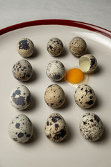 Obraz premium Quail eggs on white plate. One egg is broken.