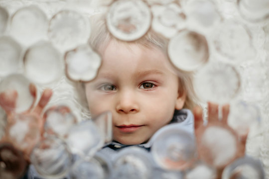 Portrait of blond toddler boy, lying under ice cubes, looking at camera