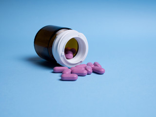 Mixed pills spilled out of the amber glass bottle. Pharmaceutical medicine tablets, capsules and pills on the blue background