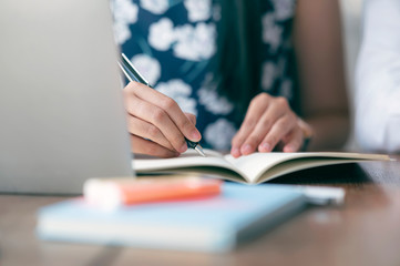 Closeup view of woman hand writing on notebook while working at home.