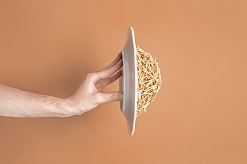 Man's hand throwing a plate of pasta on a brown background. Conceptual image