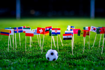 Football ball on green grass and all national flags of World Cup in Russia 2018.