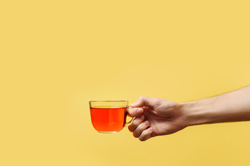 hand holding a glass tea mug on a yellow background.