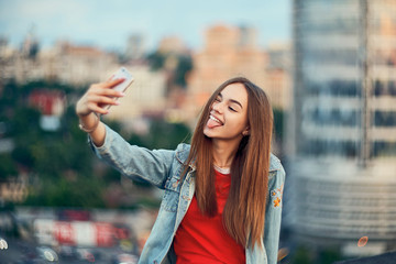 Teen girl on cityscape background making self portrait with her smart phone