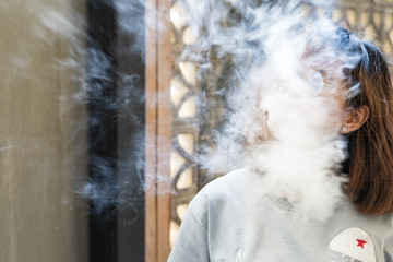 Portrait of fashion woman smoking while wearing glasses against brick wall
