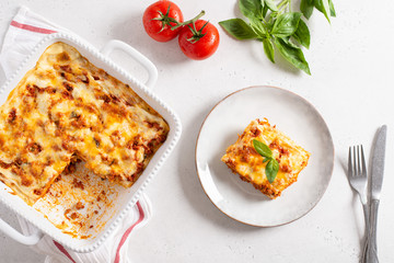 Traditional lasagna made with minced beef bolognese sauce and bechamel sauce topped with basil leaves on light background. Recipe, restaurant menu. Top view