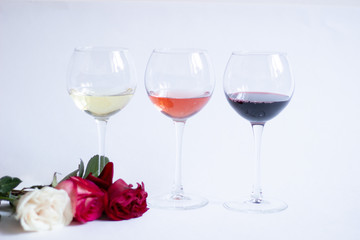 Three color wine glasses and rose flowers on white background