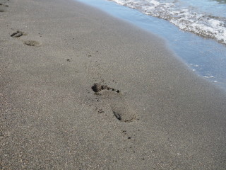 foot prints on a black sand beach with tilt-shift blur. Surf in background.