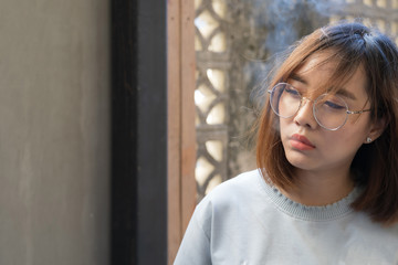 Portrait of fashion woman smoking while wearing glasses against brick wall