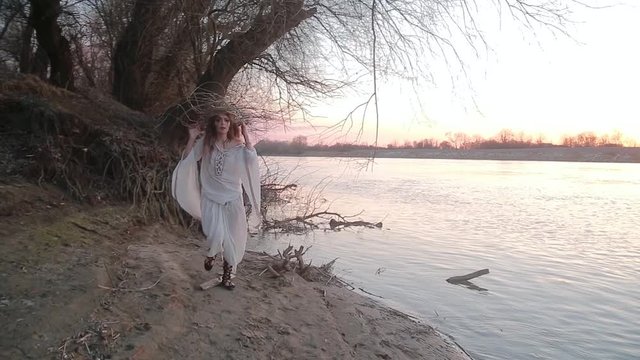 Pretty young woman in the image of witch and old Slavic costume runs on Bank of river near forest