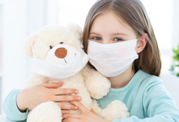 Little girl with plush teddy wearing medical masks at home