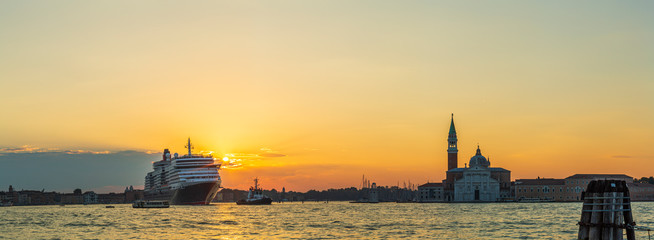Fototapeta premium A tugboat at sunrise guides a huge cruise liner along a canal in Venice