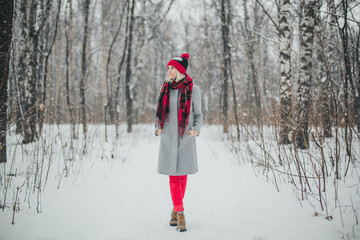 Fototapeta na wymiar Girl in gray coat and red hat walking the winter park