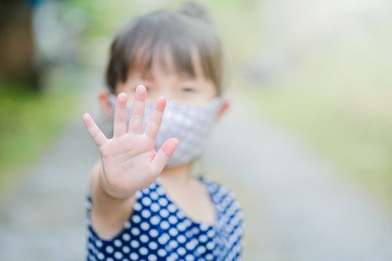 Little girl has mask protect herself from Coronavirus COVID-19,hand stop sign when child leave the house,,child with a mask on her nose for safety outdoor activity,illness or Air pollution