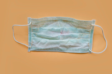 Used green surgical face mask with cosmetic stains, lipstick marks isolated on color background, cause of the spread of germs, virus or bacteria. problem of unhygienic disposal of infectious waste.