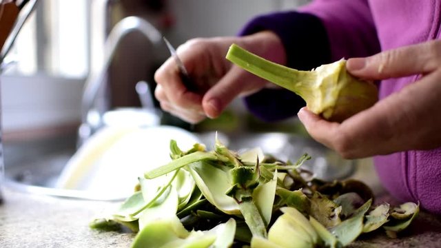 Cleaning artichoke with knife. Peeling off artichokes