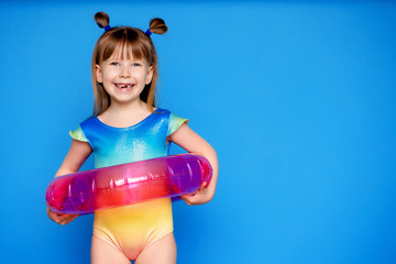 little cute girl child in a swimsuit with a swimming circle on a blue background
