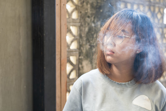 Portrait of fashion woman smoking while wearing glasses against brick wall