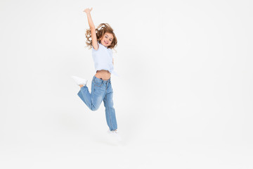 young girl in jeans jumping with happiness on a white background with copy space
