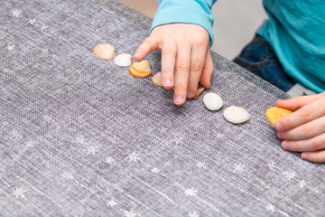 Five year old boy lining up seashells and pebbles on a table with his right hand