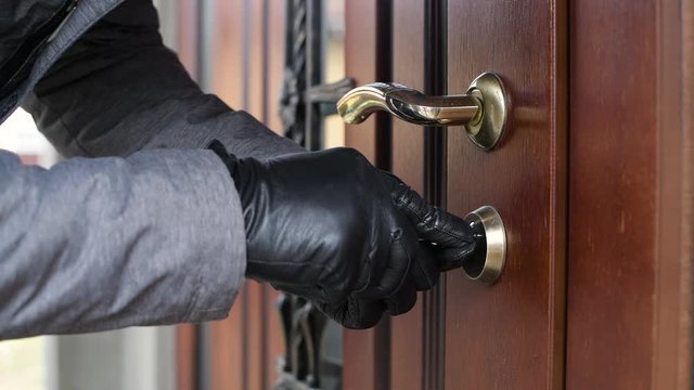 a thief in gloves opens the door lock of a private house and penetrates inside in broad daylight