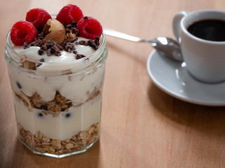 Fresh musli served with yoghurt, fresh raspberries, almonds and chocolate nibs in the jar on the table. Healthy breakfast. Close up.