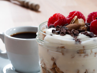 Fresh musli served with yoghurt, fresh raspberries, almonds and chocolate nibs in the jar on the table. Healthy breakfast. Close up.