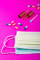 Protective face mask on pink background, pills, needle