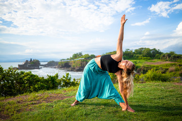 Outdoor yoga practice. Young woman practicing Utthita Trikonasana, Extended Triangle Pose. Standing asana. Tanah Lot temple, Bali, Indonesia
