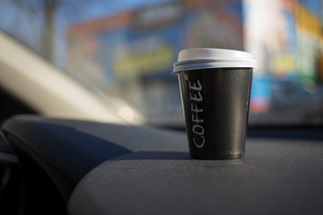 Cup of coffee is located on car console.